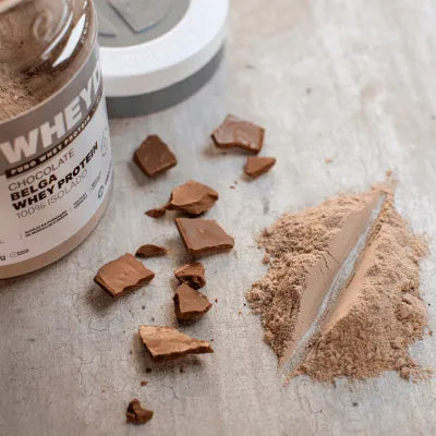 Imagem de pote de whey protein da Elemento Puro em mesa de madeira e pedaços de chocolate.